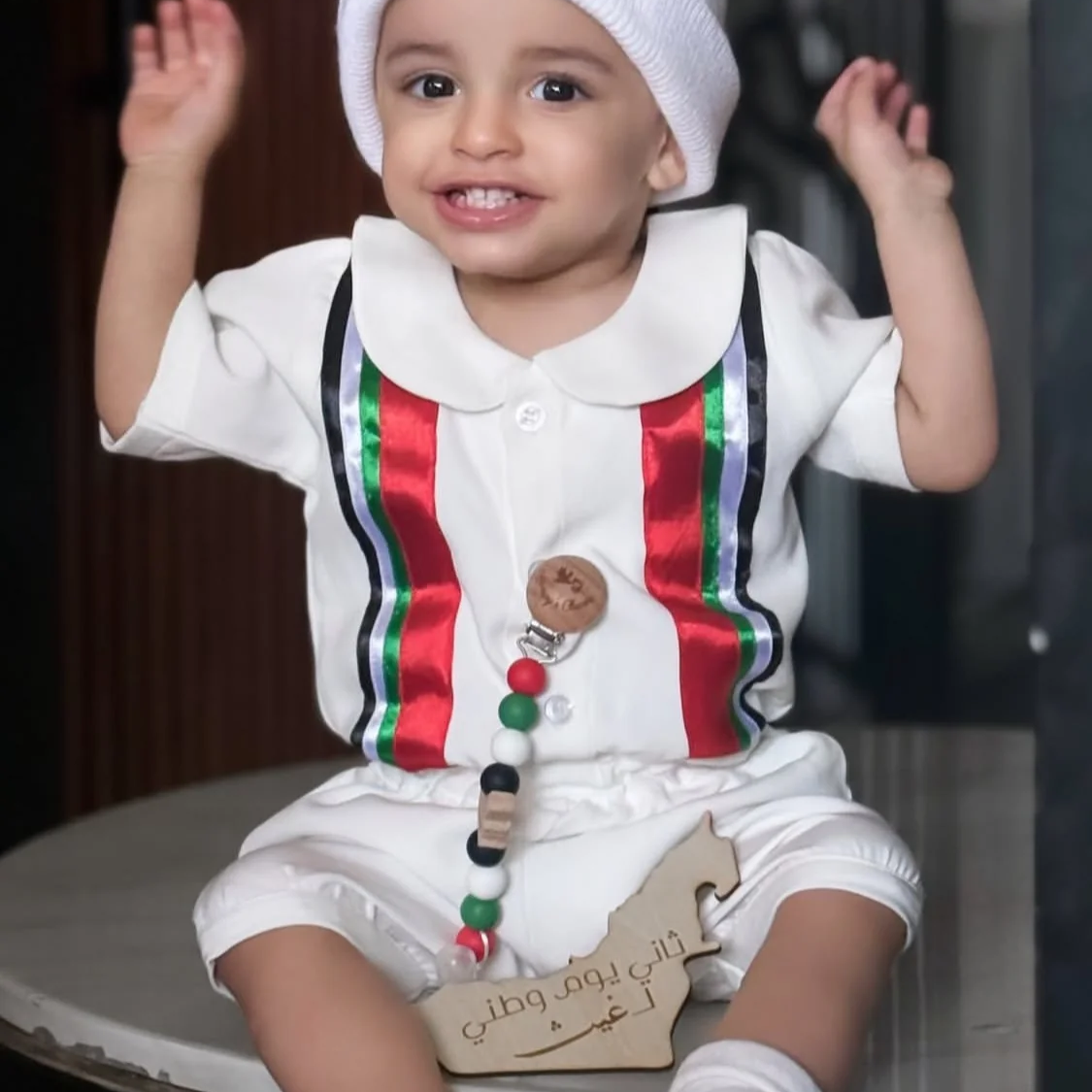 Baby wearing the loose-fit UAE National Day one-piece overall with rounded collar and UAE-colour ribbon panels